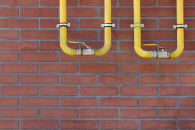 Yellow gas pipes on red brick wall outdoors, space for text