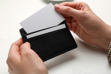 Photo of Woman holding leather business card holder with blank card at white table, closeup