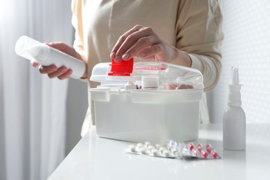 Photo of Woman opening first aid kit at white table indoors, closeup