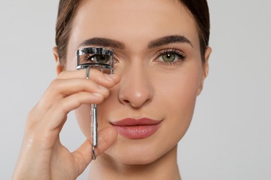 Woman using eyelash curler on white background, closeup