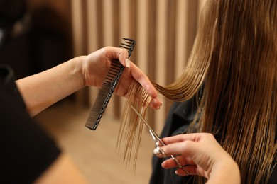 Photo of Professional hairdresser cutting girl's hair in beauty salon, closeup