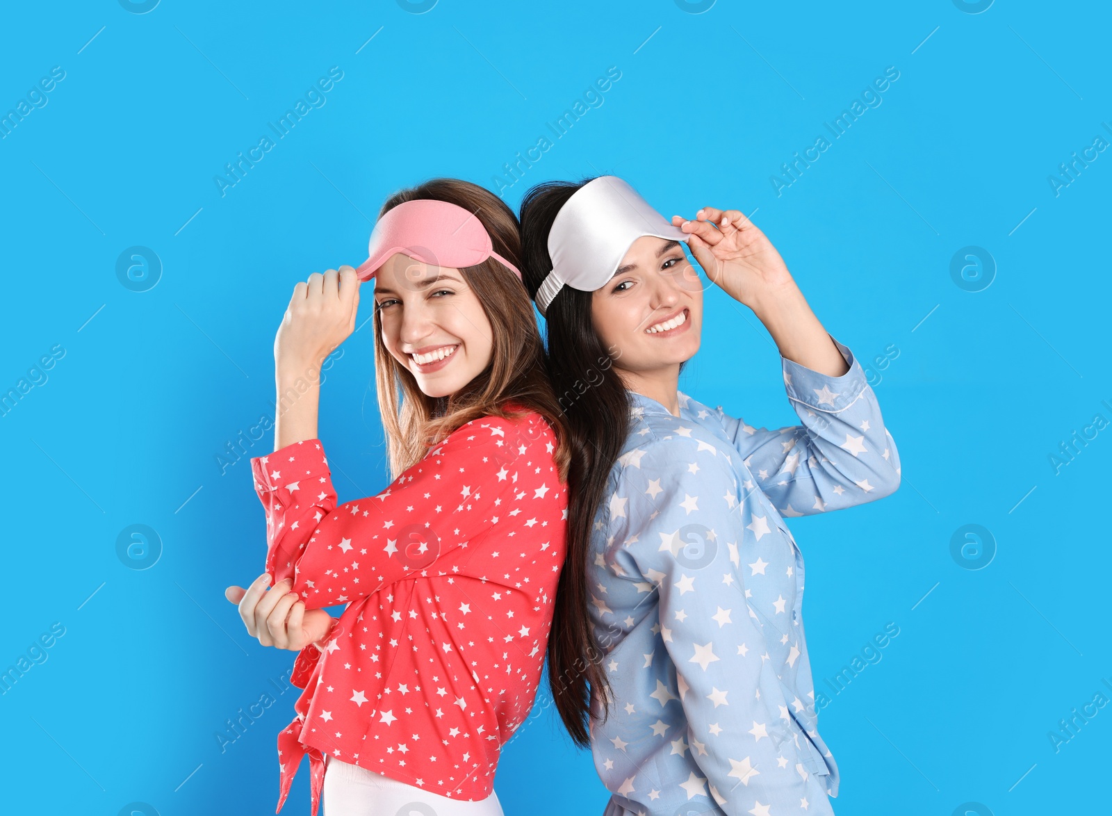 Photo of Beautiful women wearing sleeping masks on light blue background. Bedtime