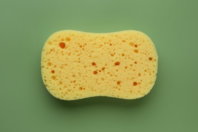 Photo of New yellow sponge on green background, top view