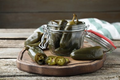 Photo of Board with pickled green jalapeno peppers on wooden table