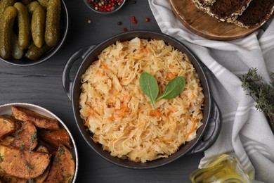 Photo of Serving pan with sauerkraut and products on black wooden table, flat lay