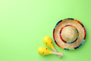 Photo of Mexican sombrero hat and maracas on green background, flat lay. Space for text