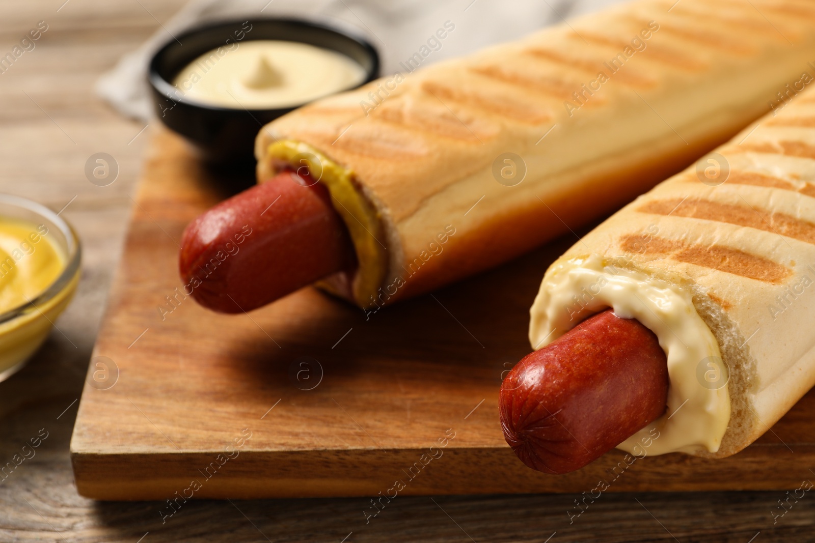 Photo of Tasty french hot dogs and dip sauces on wooden board, closeup
