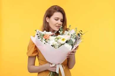 Beautiful woman with bouquet of flowers on yellow background