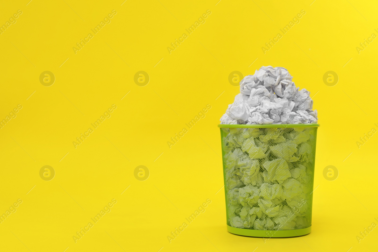 Photo of Metal bin with crumpled paper on color background, space for text