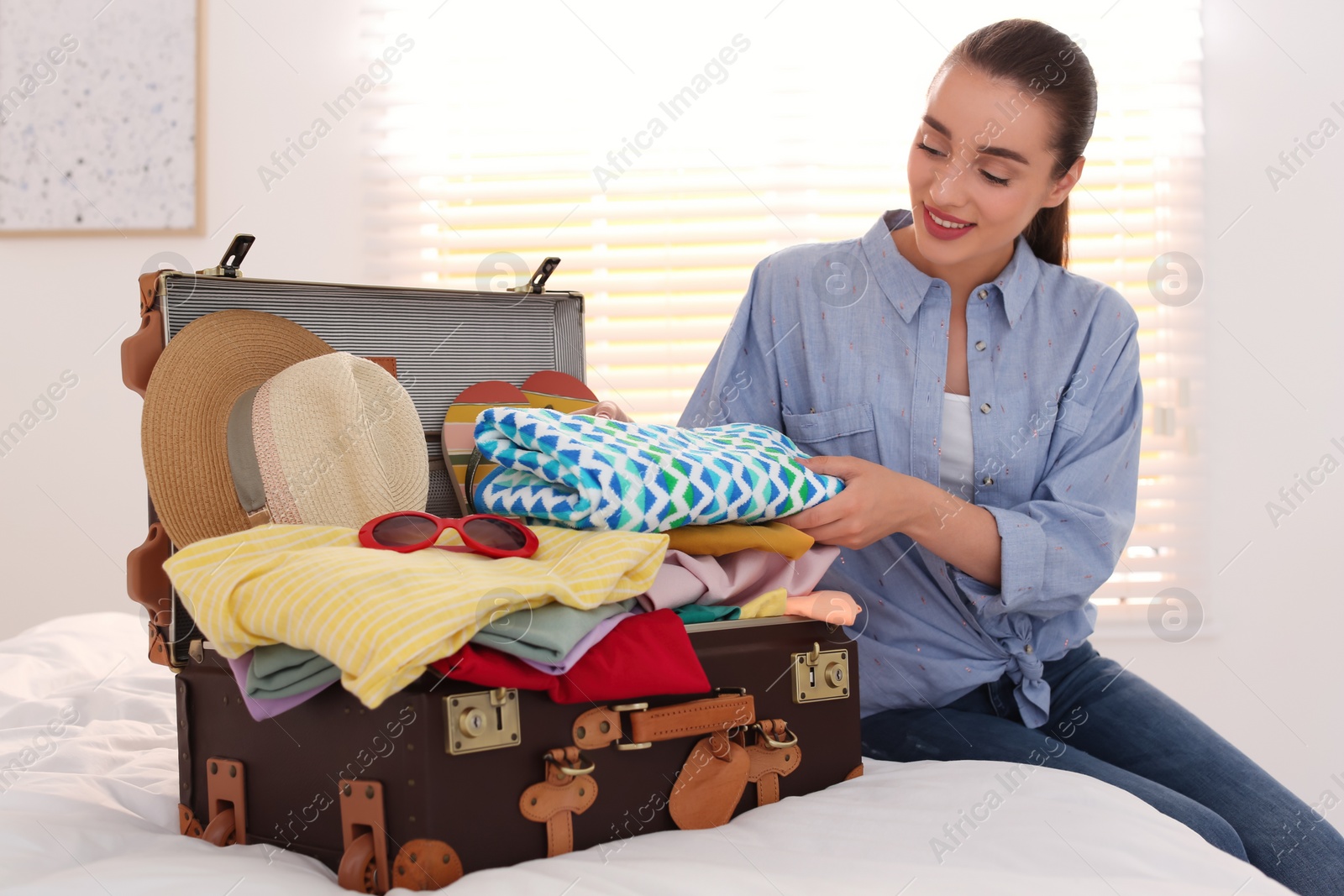 Photo of Woman packing suitcase for summer vacation in bedroom