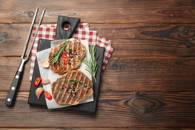 Photo of Delicious grilled pork steaks with spices and meat fork on wooden table, top view. Space for text