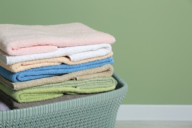 Photo of Plastic laundry basket with clean terry towels on floor near light green wall, closeup. Space for text