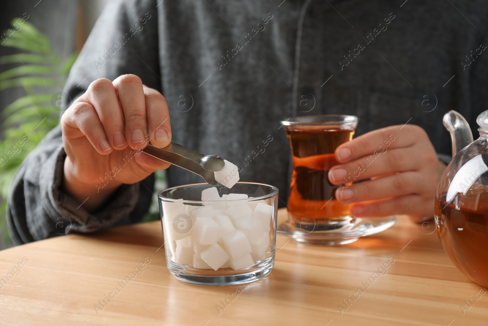 Photo of Woman adding sugar cube into aromatic tea at wooden table, closeup