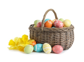 Photo of Wicker basket with painted Easter eggs and spring flowers on white background