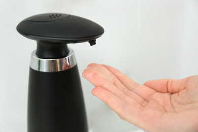 Photo of Woman using automatic soap dispenser in bathroom, closeup