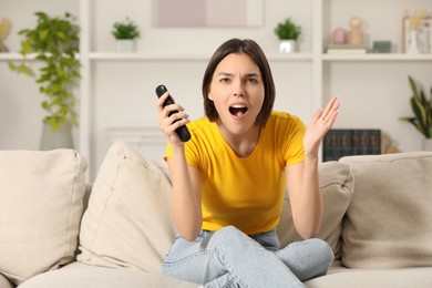 Photo of Surprised woman watching TV on sofa at home
