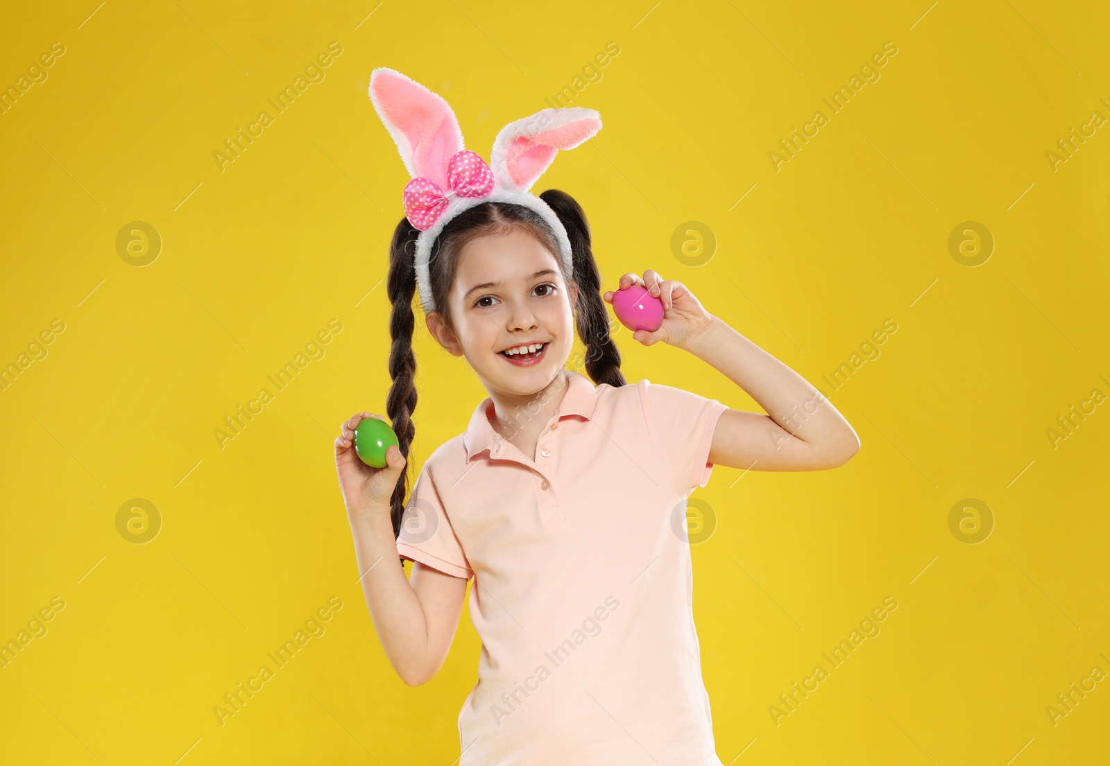 Photo of Little girl in bunny ears headband holding Easter eggs on color background