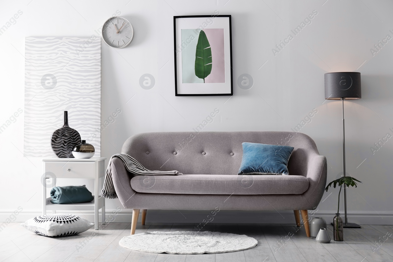 Photo of Living room interior with vases on side table and comfortable sofa near white wall