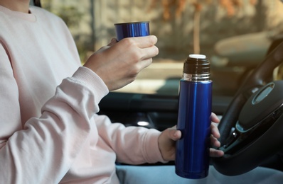 Woman with thermos on driver's seat of car, closeup 