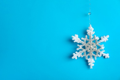 Photo of Beautiful decorative snowflake hanging on light blue background, space for text