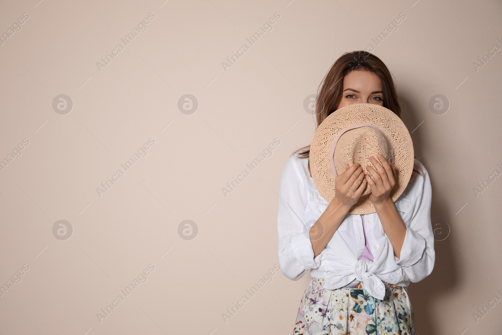 Photo of Young woman wearing floral print skirt with straw hat on beige background. Space for text