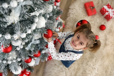 Photo of Cute little girl decorating Christmas tree at home, above view