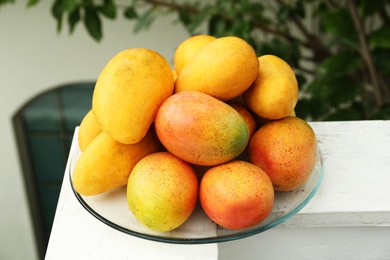 Photo of Delicious ripe yellow mangoes on glass plate outdoors