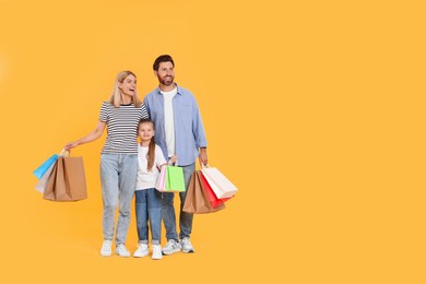 Photo of Family shopping. Happy parents and daughter with paper bags on orange background. Space for text