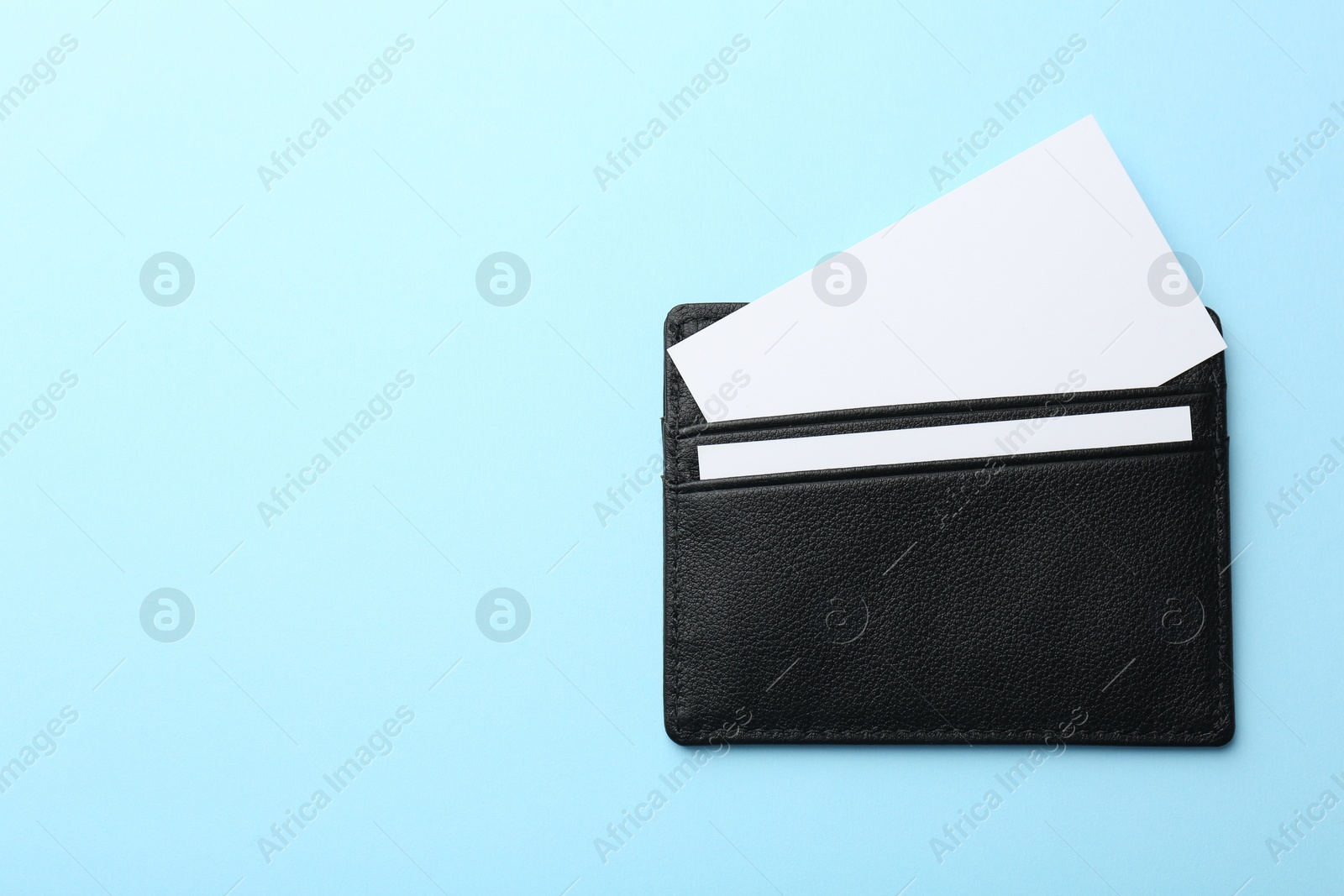 Photo of Leather business card holder with blank cards on light blue background, top view. Space for text