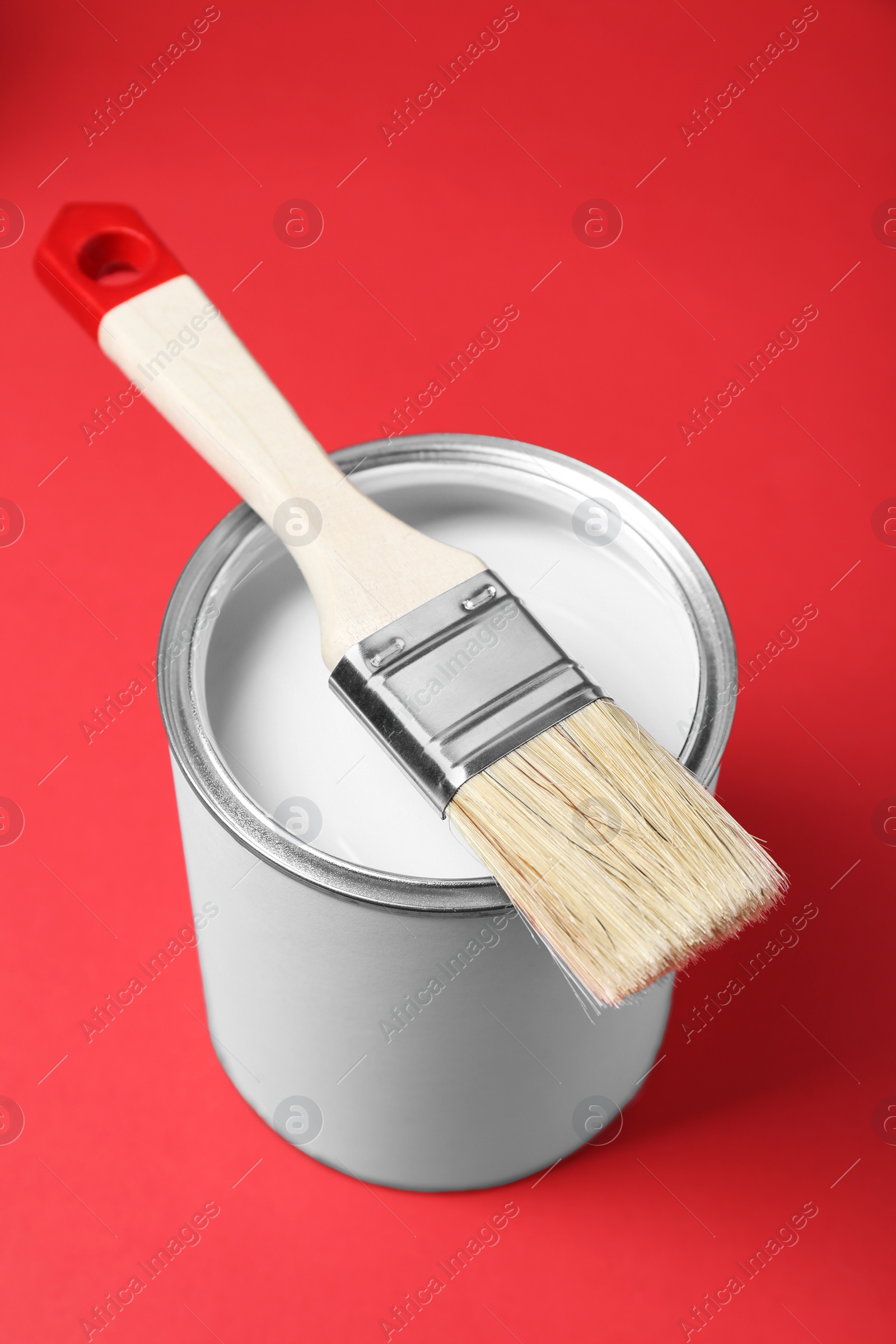 Photo of Can of white paint with brush on red background