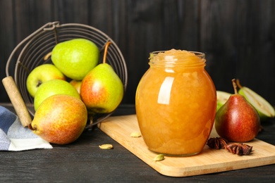 Photo of Delicious pear jam and fresh fruits on black wooden table