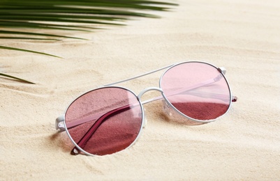 Photo of Stylish sunglasses and tropical leaf on white sand. Vacation time