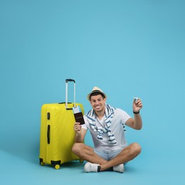 Photo of Male tourist holding passport with ticket and toy airplane near suitcase on turquoise background, space for text