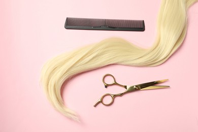 Professional hairdresser scissors and comb with blonde hair strand on pink background, top view