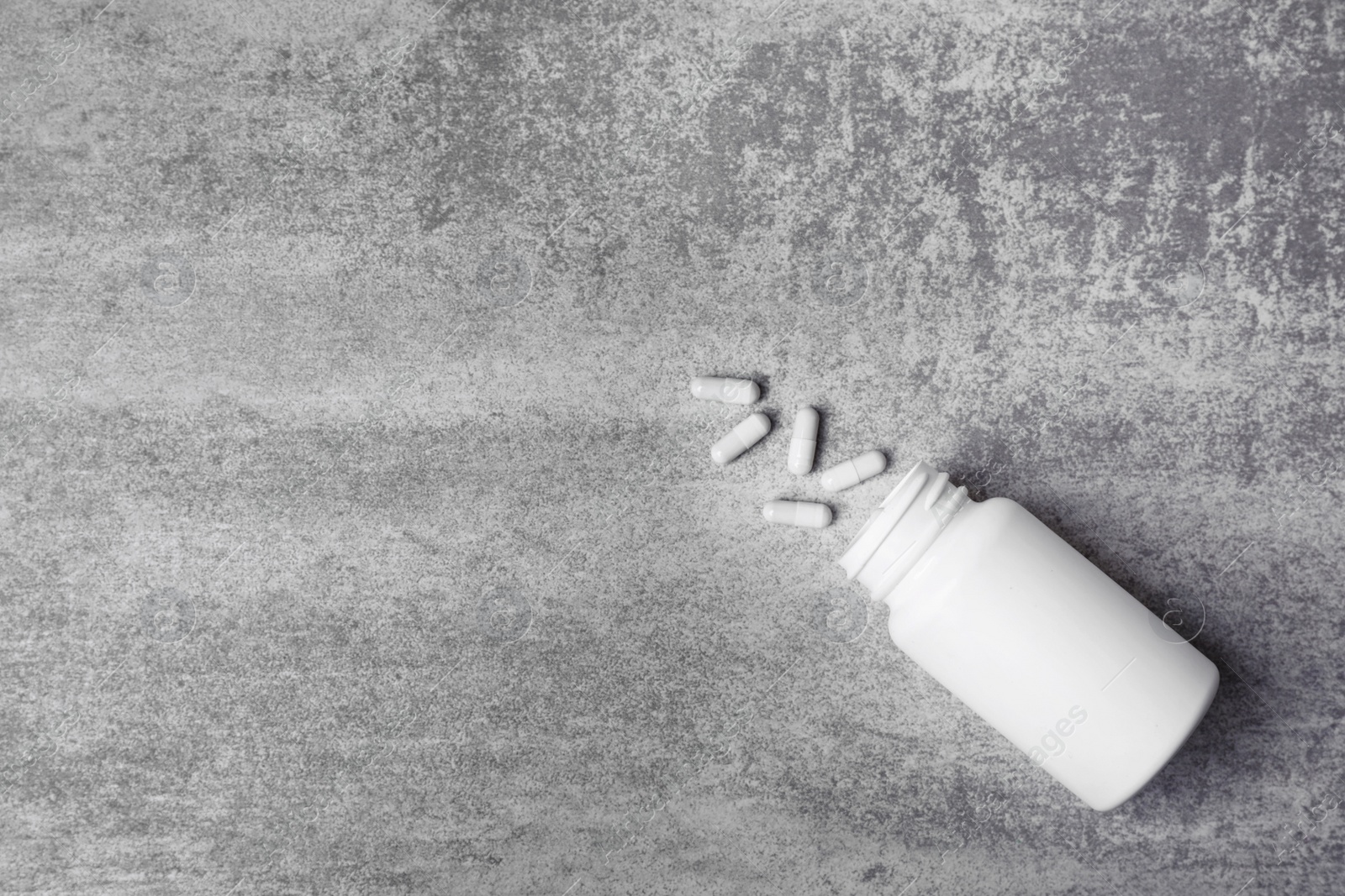 Photo of Container with white pills on grey background