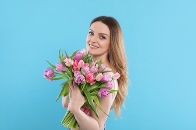 Happy young woman with bouquet of beautiful tulips on light blue background