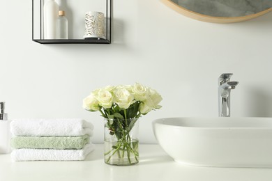 Photo of Bouquet of beautiful roses in vase and bath accessories near sink in bathroom