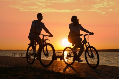 Lovely couple riding bicycles on embankment at sunset