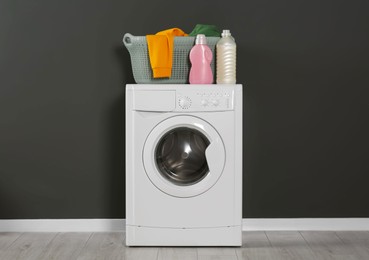 Photo of Washing machine with clothes and detergents near black wall indoors. Interior design