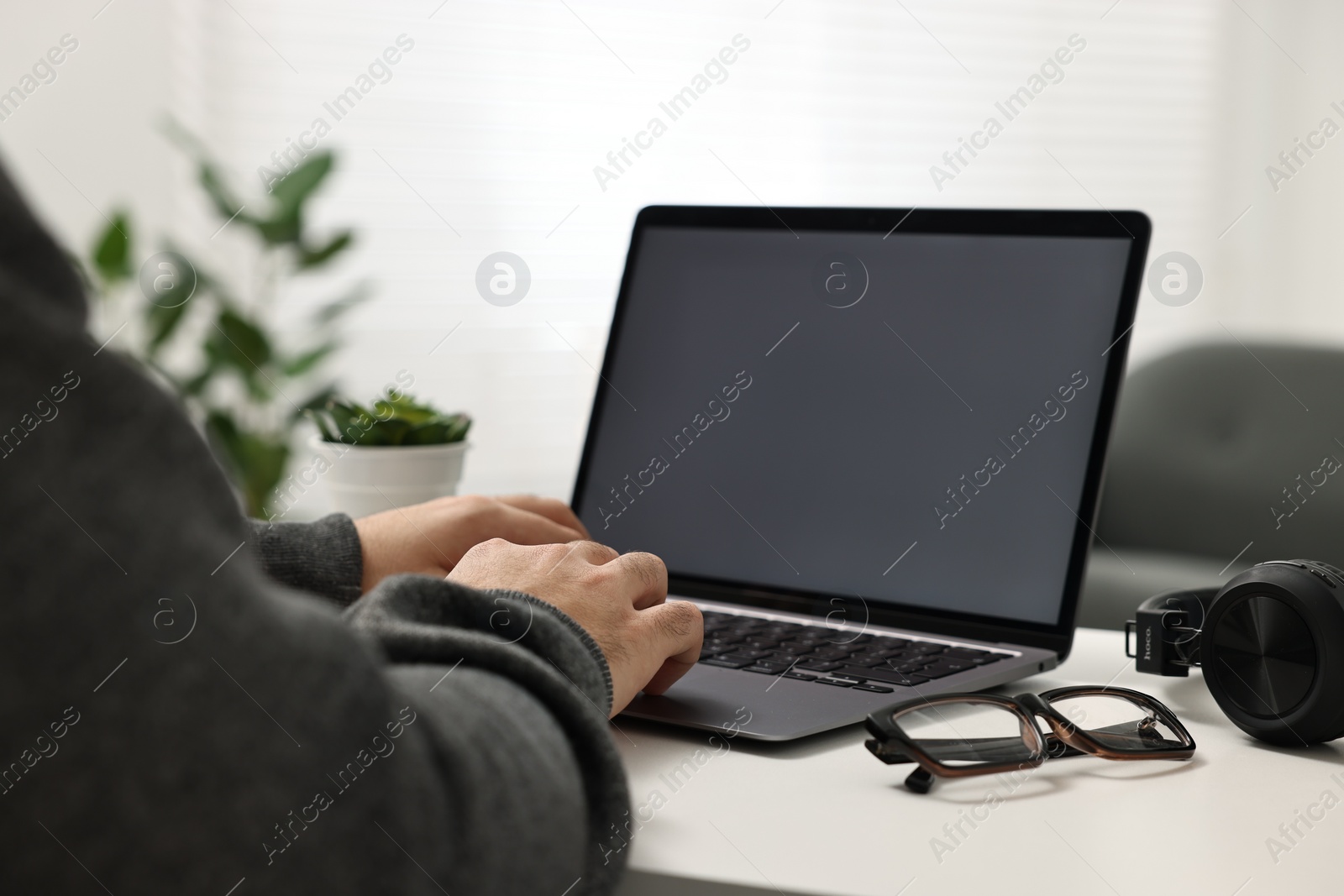 Photo of E-learning. Young man using laptop at white table indoors, closeup