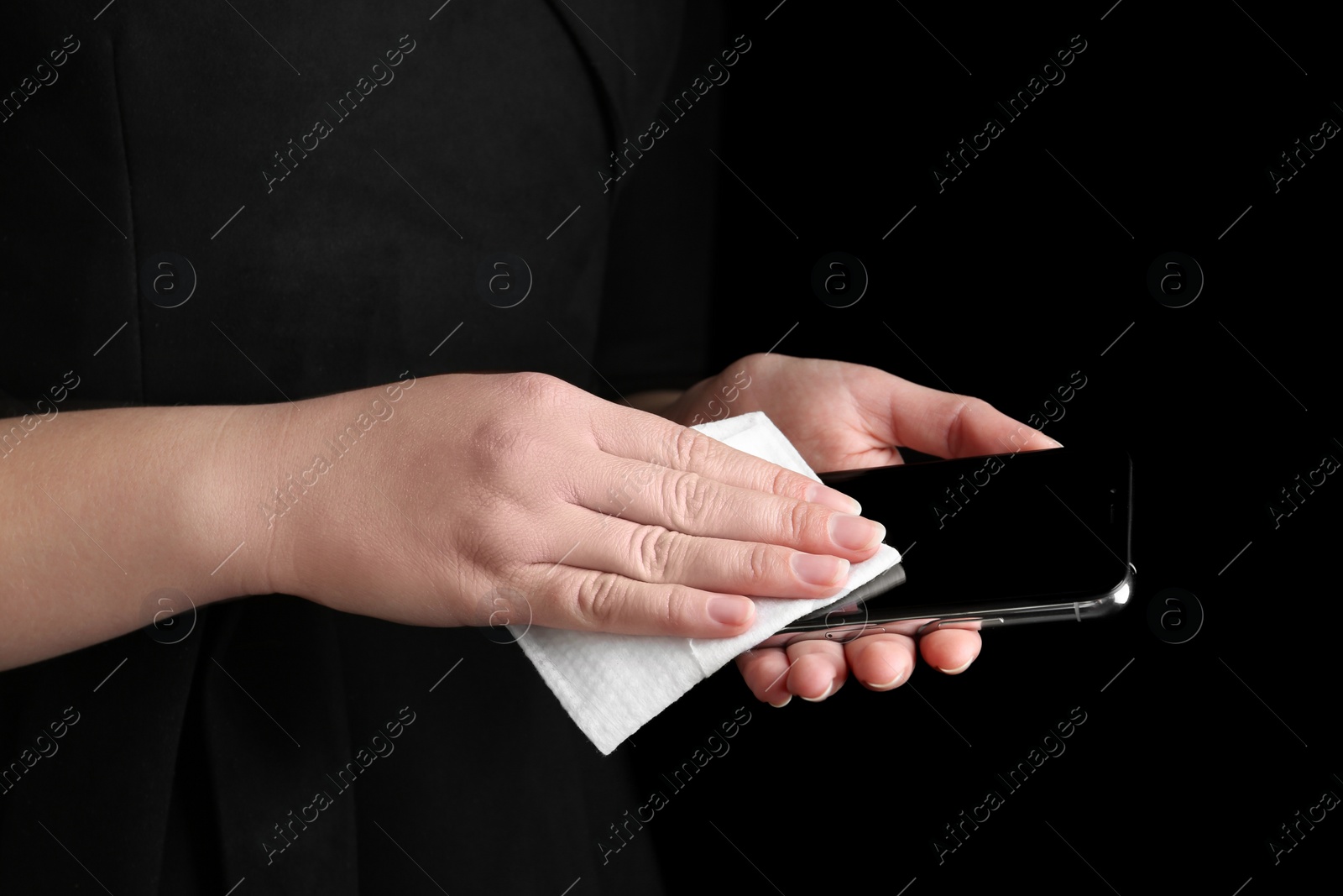 Photo of Woman cleaning mobile phone with antiseptic wipe on black background, closeup