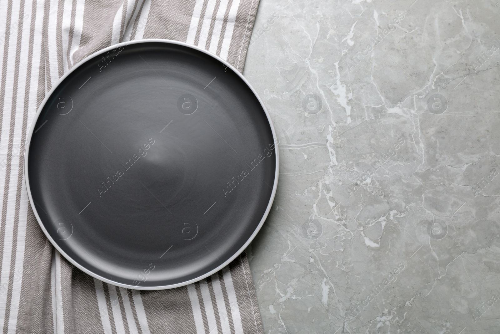 Photo of New dark plate and tablecloth on light grey marble table, top view. Space for text