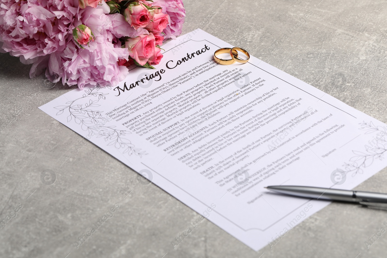 Photo of Marriage contract, golden wedding rings, pen and flowers on grey table