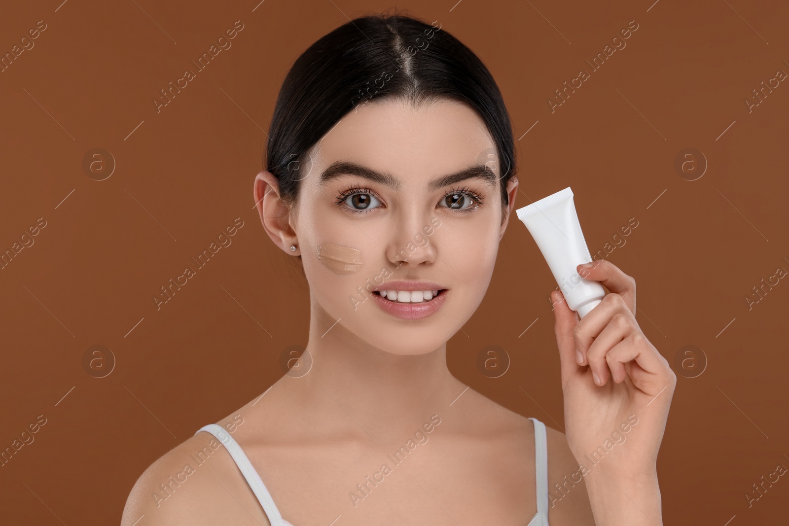Photo of Teenage girl holding tube with foundation on brown background