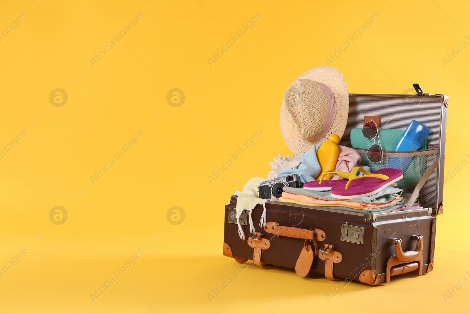 Photo of Packed vintage suitcase with different beach objects on orange background, space for text. Summer vacation