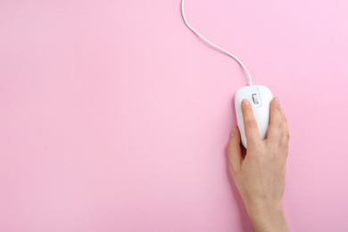 Photo of Woman using modern wired optical mouse on pink background, top view. Space for text