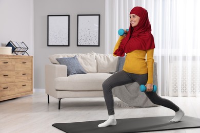 Photo of Muslim woman in hijab doing exercise on fitness mat at home. Space for text