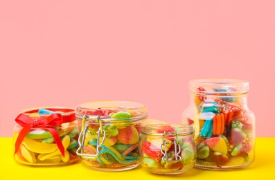 Photo of Tasty colorful candies in glass jars on yellow table against pink background