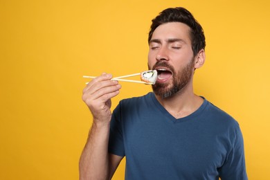 Handsome man eating sushi roll with chopsticks on orange background