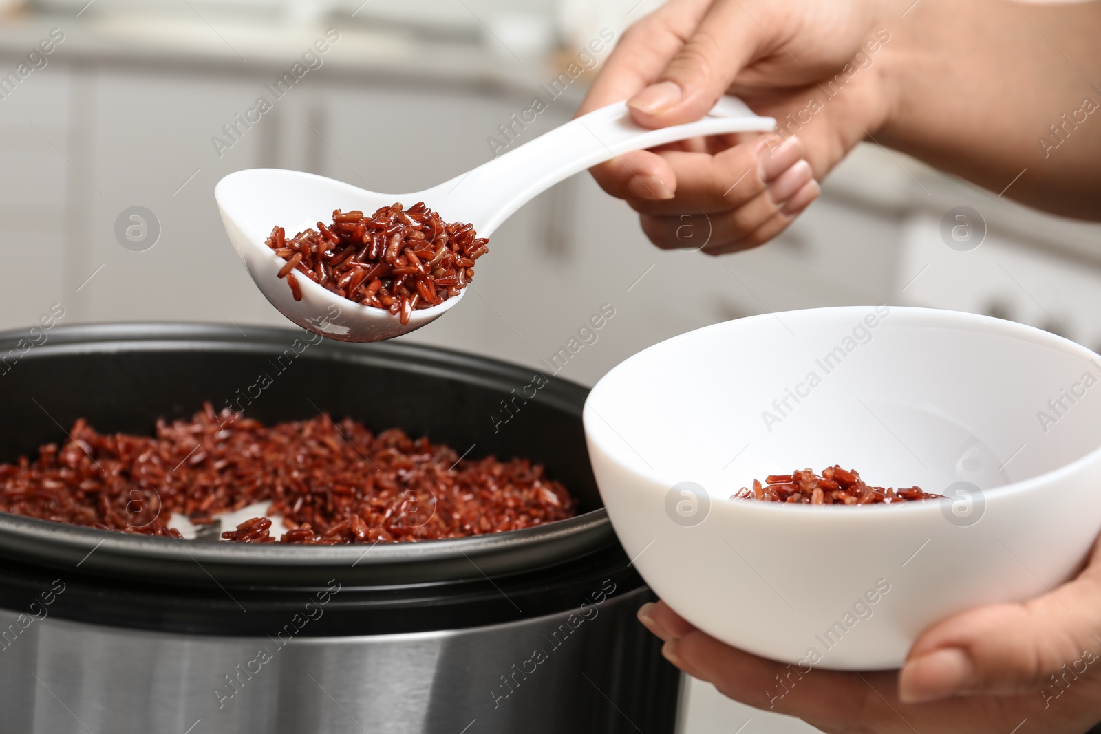 Photo of Woman putting brown rice into bowl from multi cooker in kitchen, closeup